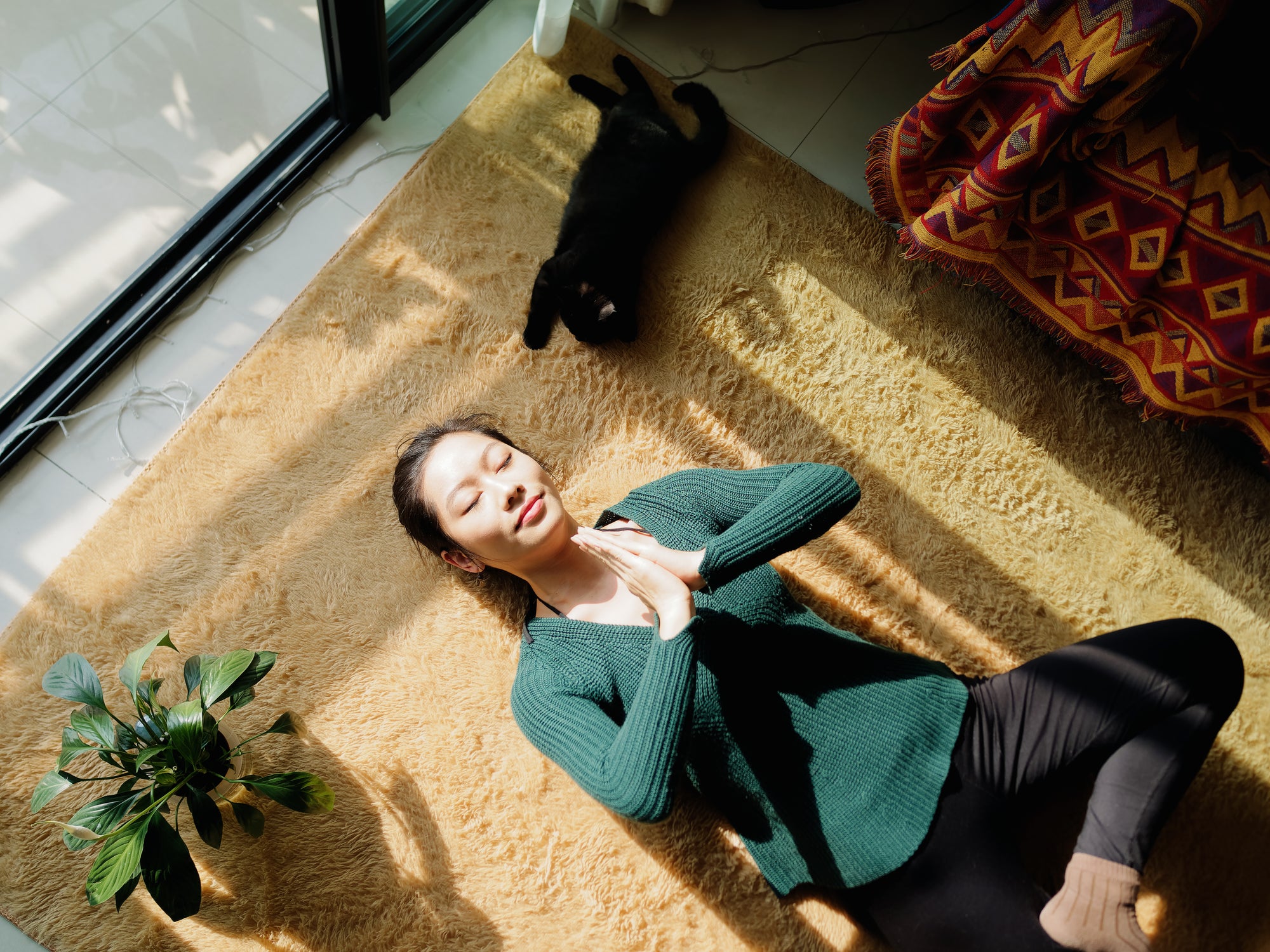 a woman meditating lying on the floor with a black cat beside her